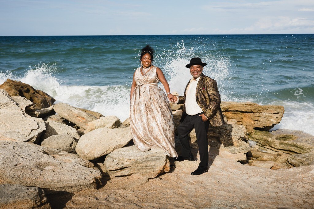 Kelechi and Rhonda on the rocks as a wave crashes behind them